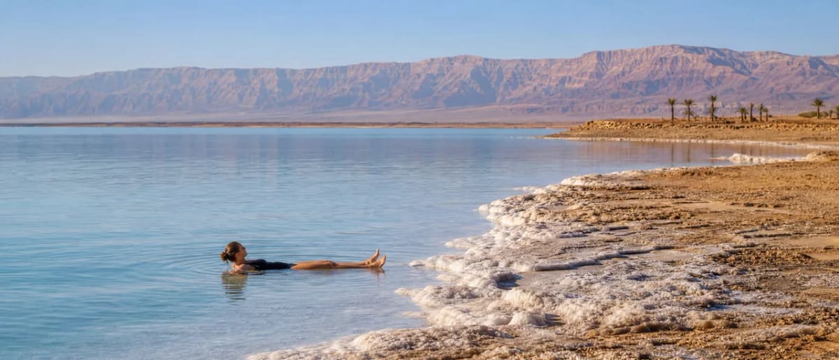 مسافر يطفو بسهولة في مياه البحر الميت الزرقاء الغنية بالمعادن والجبال في الخلفية